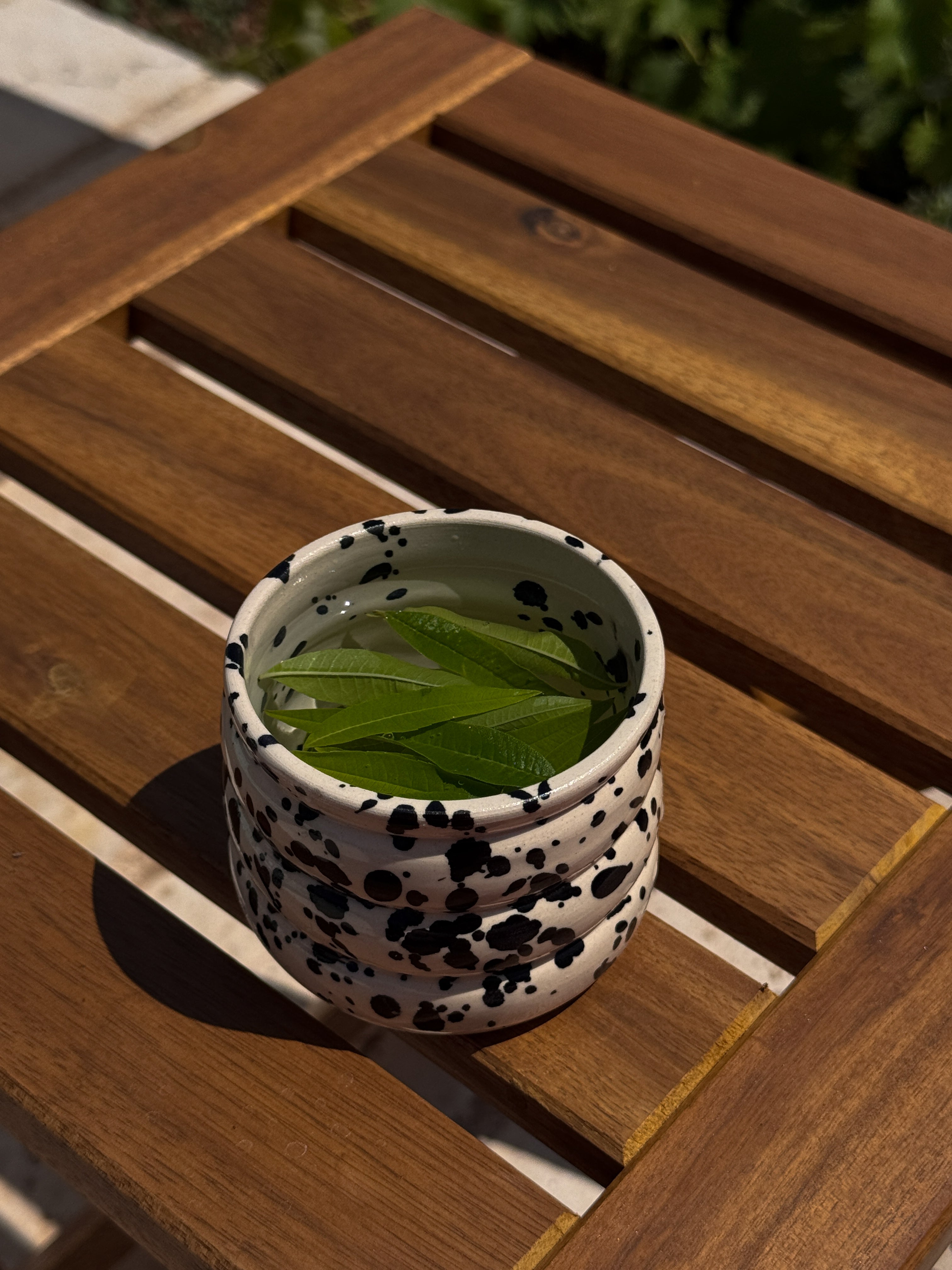 Puglia mok beige keramiek met zwarte spikkels gevuld met verveine thee op een bruine tafel