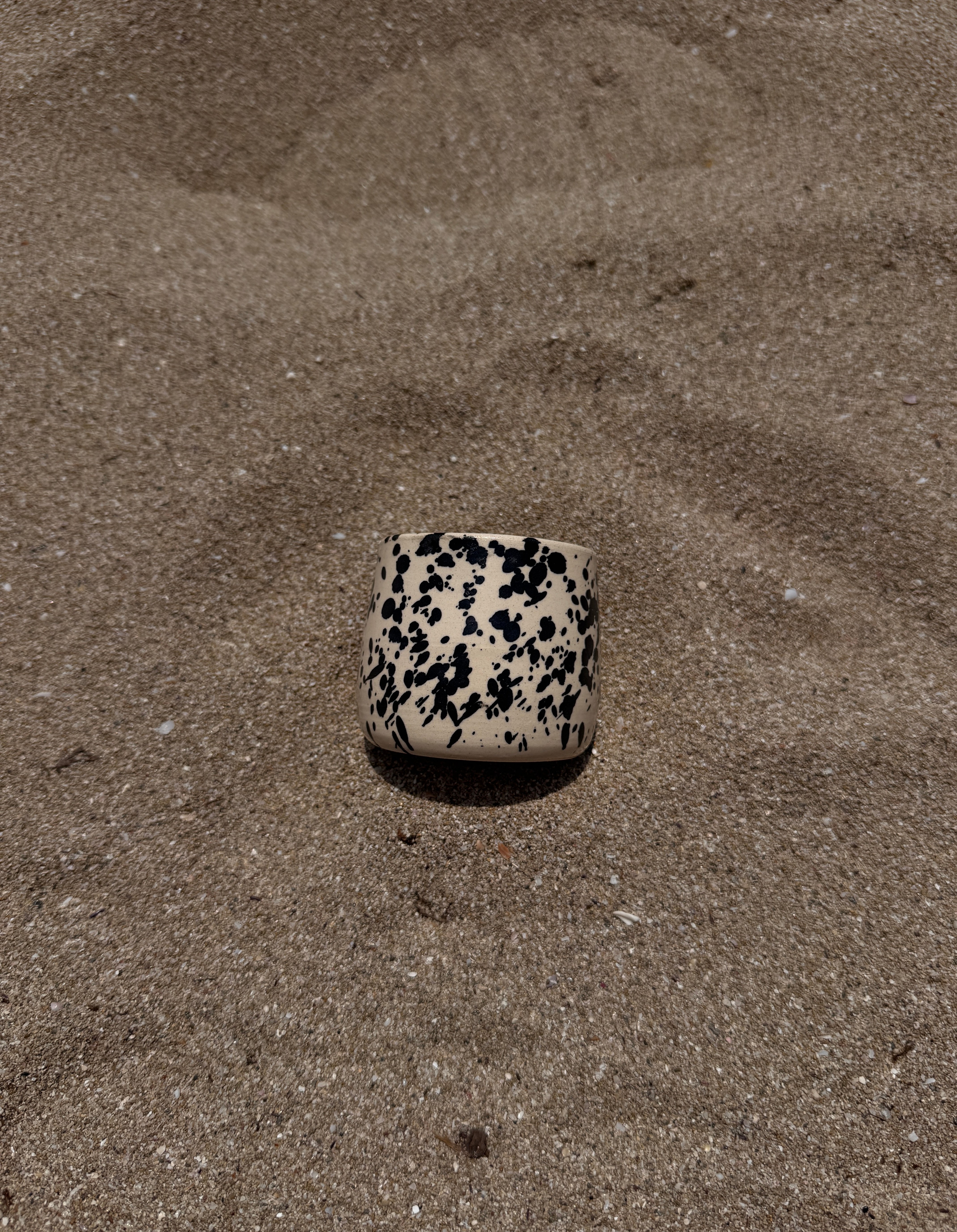 Puglia mok klein egaal beige keramiek met zwarte spikkels liggend op het strand
