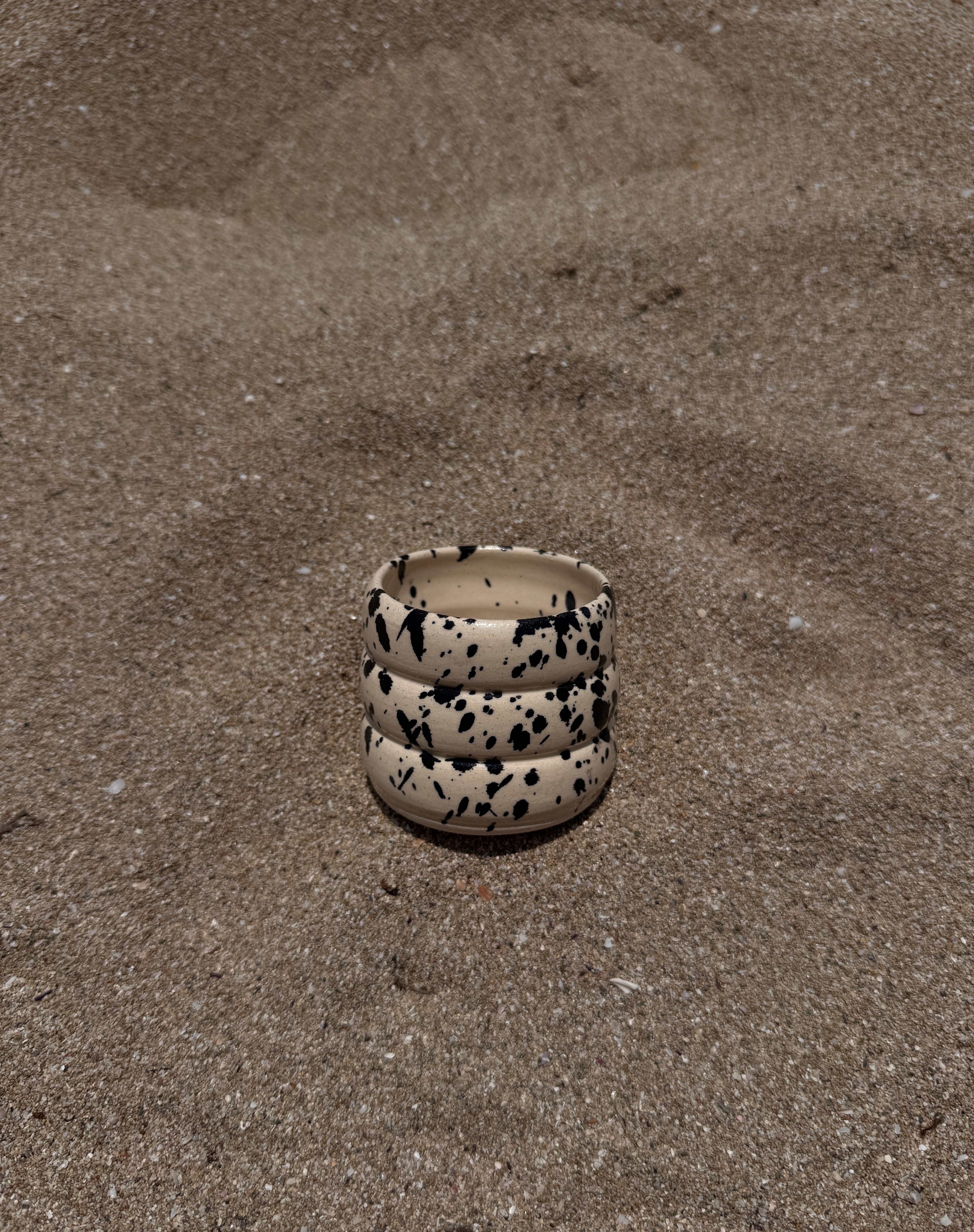 Puglia mok klein ribbel grof handgemaakt keramiek beige basis met zwarte splatter liggend op het strand 